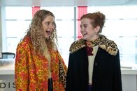 Extraordinary – Jen (Máiréad Tyers, r.) und ihre Freundin Carrie (Sofia Oxenham, l.) stehen aufgeregt in einem lichtdurchfluteten Empfangsbereich – voller Freude und Erwartung.