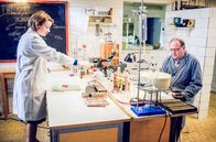 Charité – Hausmeister Fritz "Pflaster" (Uwe Preuss, r.) besucht Dr. Ella Wendt (Nina Gummich, l.) im Labor. Er hat sich bei der Arbeit am Finger verletzt.