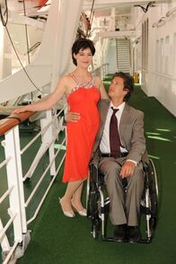 Das Traumschiff – An der Reling steht Caro Setzer (Esther Zimmering) neben Roland Wagner (Kristian Kiehling), der im Rollstuhl sitzt.