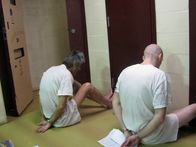 Lockdown – San Antonio, Texas: Gefangene, die mit Handschellen gefesselt auf dem Boden sitzen, während ihre Zellen durchsucht werden.