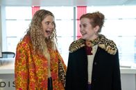Extraordinary – Jen (Máiréad Tyers, r.) und ihre Freundin Carrie (Sofia Oxenham, l.) stehen aufgeregt in einem lichtdurchfluteten Empfangsbereich – voller Freude und Erwartung.