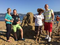 Verrückt nach Meer – Gruppenfoto mit Sandburg und Entertainment-Managerin Cori, dem Zweiten Offizier Christian, Reiseleiter Bernd und dem Vizeweltmeister im Sandburgenbauen.