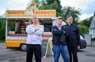 Mord mit Aussicht – Hans Zielonka (Michael Hanemann, M.), Pastor Puttermann (Johannes Rotter, r.) und Hubert (Matthias Komm, l.) stehen vor Huberts Hähnchenwagen und schauen zum "Pascha Grill", wo die Hindus ihren Gottesdienst feiern.