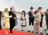 Kir Royal – Standesgemäß wird die Königin von Mandalia (Michaela May, l) vom Ministerpräsidenten (Georg Marischka) auf dem Flughafen in Empfang genommen. Herbie (Dieter Hildebrandt, r) ist dabei voll in Aktion.