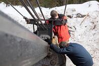 Holzfäller extrem – Aaron working outside fixing machinery, with assistance from another employee.