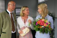 Die Rosenheim-Cops – Im Namen von Polizeichef Achtziger (Alexander Duda, l.; mit Karin Thaler, m.) hat Mitarbeiterin Lange (Sarah Thonig, r.) ein Geschenk für Sekretärin Stockl organisiert.