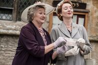 Father Brown – Mrs McCarthy (Sorcha Cusack, l.) und Margaret Cartwright (Elizabeth Berrington, r.) präsentieren stolz den Scheck, der es ermöglicht, jedem Kind in Kembleford ein Buch aus der mobilen Bücherei kostenlos zur Verfügung zu stellen.