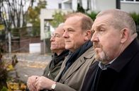 Tatort (WDR) – Rheinblick: Die Kommissare Max Ballauf (Klaus J. Behrendt, l) und Freddy Schenk (Dietmar Bär, r) sitzen mit Politiker Peter Wagner (Bernhard Schütz, M) auf einer Bank vor dessen Villa.