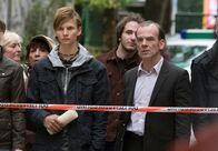 Tatort – NDR Fernsehen TATORT, "Todesstrafe" Uhr. Hauptkommissar Andreas Keppler (Martin Wuttke, rechts) ist gerade in Leipzig angekommen und beobachtet von außen die Situation am Tatort. Auch Max Lornsen (Joseph Bundschuh, links) der zu den Jugendlichen gehört, die mit Hans Freytag ihre Freizeit gestaltet haben, betrachtet traurig die Szenerie.