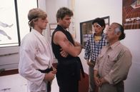 Karate Kid – Um der brutalen Schikane ein Ende zu bereiten, setzt sich Mr. Miyagi (Pat Morita, r.) für Daniel (Ralph Macchio, 2.v.r.) ein. Doch Johnny Lawrence (William Zabka, l.) und sein Karate-Meister John Kreese (Martin Kove, 2.v.r.) kennen keine Gnade.
