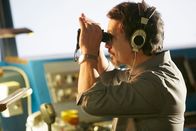 Mayday - Alarm im Cockpit – REENACTMENT - Der Betreiber von Teneriffa (gespielt von Guillermo Baez) schaut durch ein Fernglas auf die Landebahn. (Bildnachweis: Cineflex/Ian Watson)
