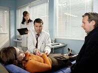 In aller Freundschaft – Nora Schubert (Oana Solomon, links) kommt, angeblich nach einem Sturz, in Begleitung ihres Mannes Kai (Steffen Münster, rechts) in die Sachsenklinik. Dr. Heilmann (Thomas Rühmann) diagnostiziert eine komplizierte Fraktur der Mittelhand. Schwester Yvonne (Maren Gilzer, 2. von links) unterstützt ihn bei der Untersuchung.