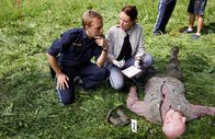 Die Rosenheim-Cops – Pathologin Mai (Sina Wilke, r.) klärt Hauptmeister Mohr (Max Müller, l.) über die Todesursache und den Todeszeitpunkt im Mordfall des Försters Denninger (Komparse) auf.