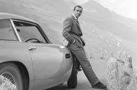 Sean Connery vs James Bond – Sean Connery als James Bond neben seinem Aston Martin DB5 in einer Szene des Films „Goldfinger“ aus dem Jahr 1964