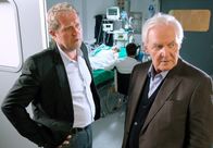 Der Winzerkönig – MDR Fernsehen DER WINZERKÖNIG III. STAFFEL, FOLGE 31, "Die Krise" Uhr. Nach dem schrecklichen Autounfall liegt Claudia (Susanne Michel, im HG.) im Koma. Thomas (Harald Krassnitzer, l.) verdächtigt den behandelnden Arzt einer unzureichenden Behandlung. Er teilt Gottfried (Wolfgang Hübsch, r.) mit, wie kritisch Claudias Zustand ist.