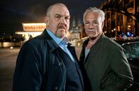 Tatort – Die Kommissare Max Ballauf (Klaus J. Behrendt, rechts) und Freddy Schenk (Dietmar Bär) an der Wurstbraterei, neben der Hohenzollernbrücke mit dem Kölner Dom im Hintergrund.
