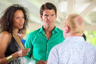 Death in Paradise – Lauren Campese (Vinette Robinson, l.) und Marc Campese (Tristan Gemmill, M.) genießen noch die Feier bei Leo Pascal (Adrian Scarborough, r.). Doch schon bald gerät Lauren ins Visier der Polizei. Sie kannte das Opfer besser, als sie zugeben möchte.