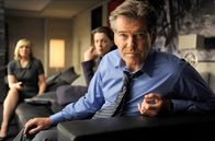 Der Ghostwriter – Lang (Pierce Brosnan, r.) erfährt zusammen mit seiner Frau Ruth (Olivia Williams, Mitte) und seiner Assistentin Amelia (Kim Cattrall, l.) aus den Nachrichten, dass gegen ihn wegen Kriegsverbrechen während des Irakkrieges ermittelt wird.
