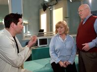 In aller Freundschaft – Dr. Brentano (Thomas Koch, links) erklärt Ilse Richter (Karin Ugowski) und Arthur Vogelsang (Hans Teuscher), dass Arthur einen Bruch im Zwerchfell hat und dass so der Magen in den Brustkorb gleitet. Ilse glaubt, dass sie es mit dem Kochen übertrieben hätte und macht sich Vorwürfe.