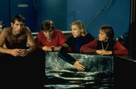 Der weiße Hai III – Sean (John Putch, l.), Mike (Dennis Quaid, 2.v.l.), Kathryn (Bess Armstrong, 2.v.r.) und Kelly (Lea Thompson, r.) beratschlagen, wie sie gegen den Hai vorgehen sollen.