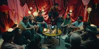 neoriginal: Doppelhaushälfte – Beim Rollenspiel "Werwölfe" beschwört Spielleiter Theo (Benito Bause, M.) in seinem mit roten Tüchern und Lampions dekorierten Wohnzimmer alle Teilnehmer. Von links: Oma Thuy (Tuyet Linh Phung), Tracy (Minh-Kai Phan-Thi), Andi (Milan Peschel), Gesa (Nina Proll), Martin (Johannes Allmayer), Mari (Maryam Zaree), Keks (Dillan White), Zoe (Helena Yousefi), Rocco (Hoang Minh Ha), Wörner (Peer Martiny), Eckner (Aysima Ergün).