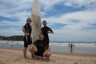 Verrückt nach Meer – Entertainment-Managerin Cori, zweiter Offizier Christian Baumann und Mitglied des Showensembles Esther posieren mit Surfbrett in Buzios, Brasilien.