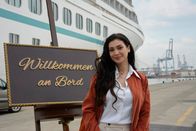 Das Traumschiff – Tänzerin Kathrin Bree (Paola Maria) steht vor einem Schild "Willkommen an Bord".