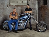 American Chopper – Paul Sr. sits on Paul Jr.'s blue auction bike while Paul Jr. stands behind. As seen on AMERICAN CHOPPER.