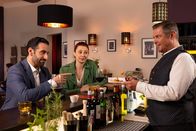 Die Rosenheim-Cops – Controller Donato (Paul Brusa, l.), Kommissarin Schubert (Sophia Schiller, M.) und Wirt Jo Caspar (Christian K. Schaeffer, r.) unterhalten sich über die laufenden Ermittlungen.