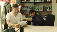 All In – Jamu (Daniel Popat, re.) stellt sich vor dem Mitarbeiter (Daniel Wassermann) der Ausländerbehörde unwissend.