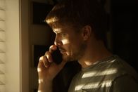Tödliche Stille – A man looks out of a window while talking on the cell phone.
