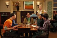 The Big Bang Theory – Priya (Aarti Mann, 2.v.r.) ist wieder in der Stadt. Bei einem gemeinsamen Abendessen erfahren Sheldon (Jim Parsons, l.), Rajesh (Kunal Nayyar, 2.v.l.), Penny (Kaley Cuoco, stehend) und Howard (Simon Helberg, r.), dass Leonard (Johnny Galecki, 3.v.l.) und sie eine Beziehung eingehen wollen ...