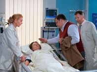In aller Freundschaft – Hans-Peter Brenner (Michael Trischan, 2. von rechts) will seiner Mutter Luise (Monika Lennartz, 2. von links) die freudige Nachricht überbringen, dass er die Stelle als Krankenpfleger bekommen hat. Dr. Heilmann (Thomas Rühmann, rechts) und Oberschwester Ingrid (Jutta Kammann) bitten ihn, seiner Mutter, die noch nicht aus der Narkose aufgewacht ist, etwas Ruhe zu lassen.