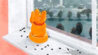 Die Tochter – Eine Glückskatze winkt einsam aus dem Fenster. Um sie herum haben sich tote Fliegen angesammelt.
