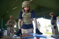 Mayday - Alarm im Cockpit – ONTARIO - RE-ENACTMENT - Investigator (played by Dmitry Chepovetsky) looks over photos from the crash in the crash site tent while military personnel (played by background performers) stand by.  