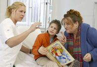 Bezaubernde Marie – Marie (Marianne Sägebrecht, re.) lenkt den kleinen Tommy (Luka Andres) ab, damit die Krankenschwester Sonja (Nina Kapust) ihm eine Spritze geben kann.