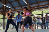 Deadly Tropics – Mélissa (Sonia Rolland, l.) muss im Rahmen der Ermittlungen an einem illegalen Boxkampf teilnehmen. Unter Aufsicht des Schiedsrichters (Rodman, M.) hat sie gegen eine starke Gegnerin (Sephora Bissoly, r.) zu kämpfen.