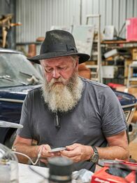 Outback Car Hunters – BMW repair – Dave in foreground sitting, tinkering.