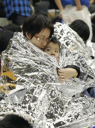 Japans Erdbebenkatastrophe – Eine Person hält ein Kind fest, das einen Katastrophenschutzmantel um den Körper trägt, in einem provisorischen Schutzraum der Aoyama Gakuin Univ. in Shibuya Ward, Tokio, 11. März 2011. Das stärkste Erdbeben der Stärke 8,8 erschütterte die nordöstliche Region an der japanischen Pazifikküste und löste einen Tsunami und Brände aus, bei denen Hunderte Menschen starben.
