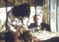 Unsere kleine Farm – Luther (David Hooks, r.), der Gehilfe von Dr. McQueen, entschuldigt sich bei dem "Wolfsmenschen" Matthew (Jonathan Hall Kovacs, l.), dass er wie ein Tier in einem Käfig hausen muss.