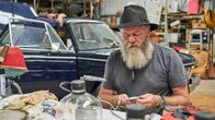Outback Car Hunters – BMW repair – Dave in foreground sitting, tinkering.