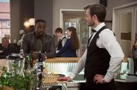 Rote Rosen – Während Hendrik (Jerry Kwarteng, l. mit Kompars:innen) an ein romantisches Candle-Light-Dinner denkt, um Britta einen Antrag zu machen, schmiedet Philip (Marc Schöttner, r.) größere Pläne für seine Schwester ...