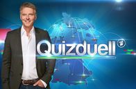 Quizduell - Olymp – Moderator Jörg Pilawa mit Logo.