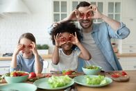 111 – Happy small african american and caucasian girls having fun with carefree european father in kitchen, posing for photo with vegetables, laughing multiracial family making funny faces grimaces.