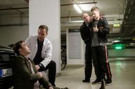 In aller Freundschaft – Als Dr. Kai Hoffmann (Julian Weigend, 2.v.li.) und der Polizist (Komparse) in der Tiefgarage eintreffen, sitzt Gesundheitsdezernent Dr. Clemens Seidel (Moritz von Zeddelmann, li.) zusammengesunken vor seinem Auto. Der Polizist nimmt den Strafgefangenen Dennis Karow (Ilja Roßbander, re.) sofort wieder in Gewahrsam.