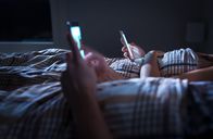 Smartphone Zombies – Langes entferntes Ehepaar ignoriert einander, das nachts im Bett liegt, während es Mobiltelefone benutzt. Smartphone-Drogenabhängiger. Besessene und abgelenkte Mann und Frau SMS. Abhängigkeit von sozialen Medien und Technologie.