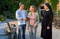 Um Himmels Willen – Anne Steiner (Luise Hart, M.) spricht mit Schwester Hanna (Janina Hartwig, r.) über ihre Hochzeit, als plötzlich ihr zukünftiger Mann Bastian Mitterhammer (Justus Johanssen, l.) mit einem schicken Cabrio angebraust kommt und ihr wertvollen Schmuck überreicht.