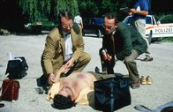 Kommissar Rex – Kriminalassistent Stockinger (Karl Markovics, r.) und der Gerichtsmediziner Dr. Graf (Gerhard Zemann, l.) untersuchen die Leiche eines Mannes, der in einer Mülltonne gefunden wurde. Kommissar Moser glaubt, dass ein Verbrecher-Ring hinter dem Mord steckt ...