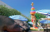 Athleticus – Schwer bepackt versucht die Giraffe, den anderen Tieren Strandzubehör zu verkaufen.