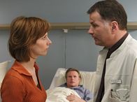 In aller Freundschaft – Susanne Frenzen (Anka Baier) hält die Diagnose für eine Farce, um die drohende Klage abzuwenden. Dr. Heilmann (Thomas Rühmann, re.) versucht ihr zu erklären, dass die damalige Operation und die heutige Diagnose nichts miteinander zu tun haben. Rüdiger Frenzen (Konstantin Graudus, mi.) erkennt seine Frau nicht wieder.